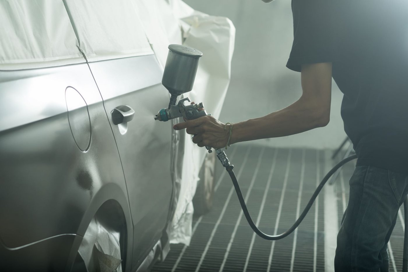 Technician spraying fresh paint onto a car panel