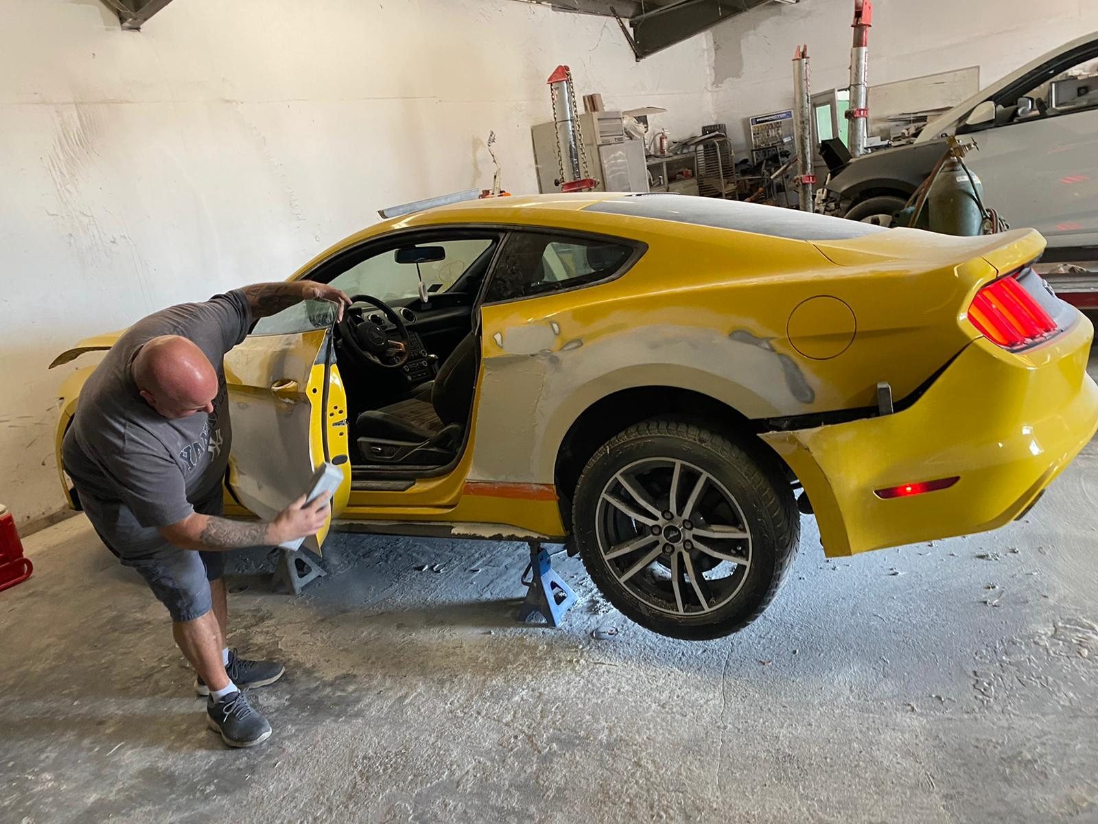 A yellow Mustang getting body work in the bay